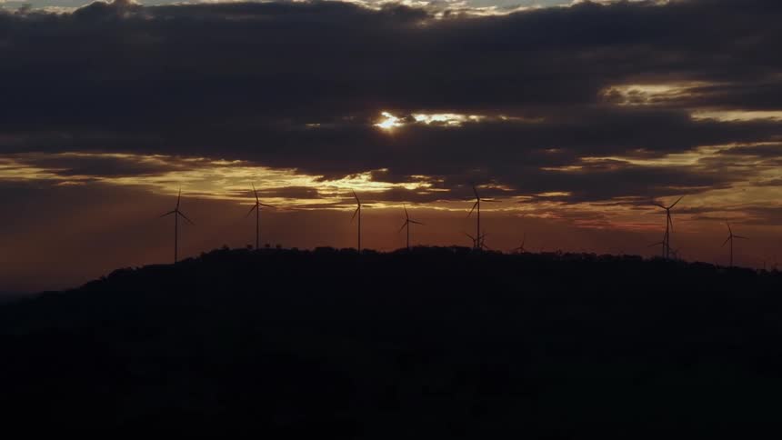 Sun setting out west behind mountain littered with wind turbines.