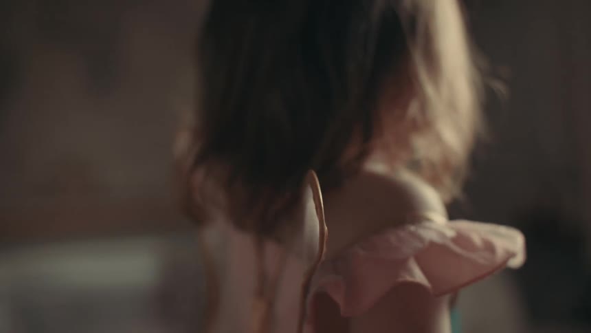A young child dressed in a pink gown with wings on the back dances around