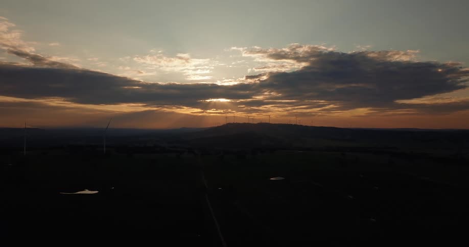 Sunset backlights wind farm as a solar farm is revealed in the foreground
