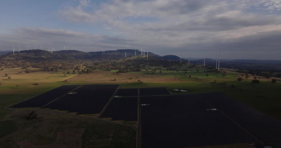 The fields are covered in solar panels with windmills on the hills