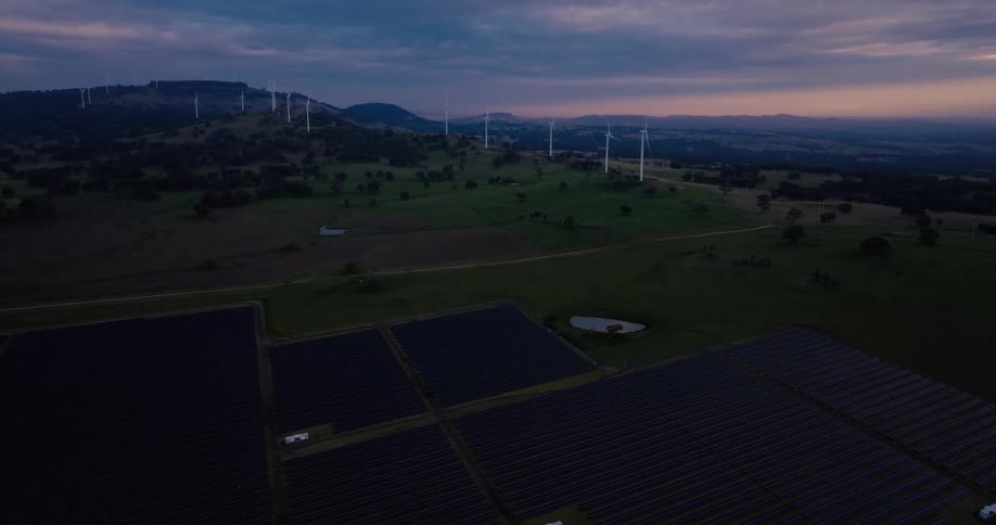 A landscape shows a combination of a solar farm and wind turbines under a twilight sky