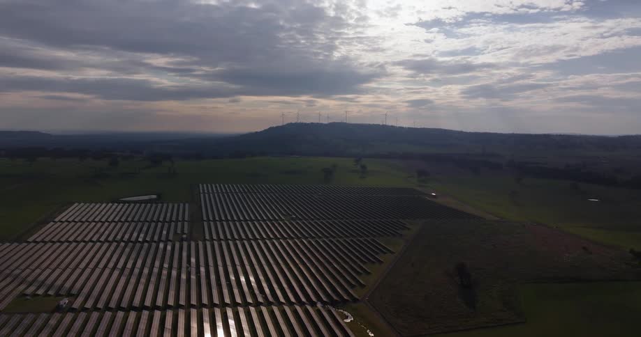 A landscape shows a combination of a solar farm and wind turbines under a twilight sky
