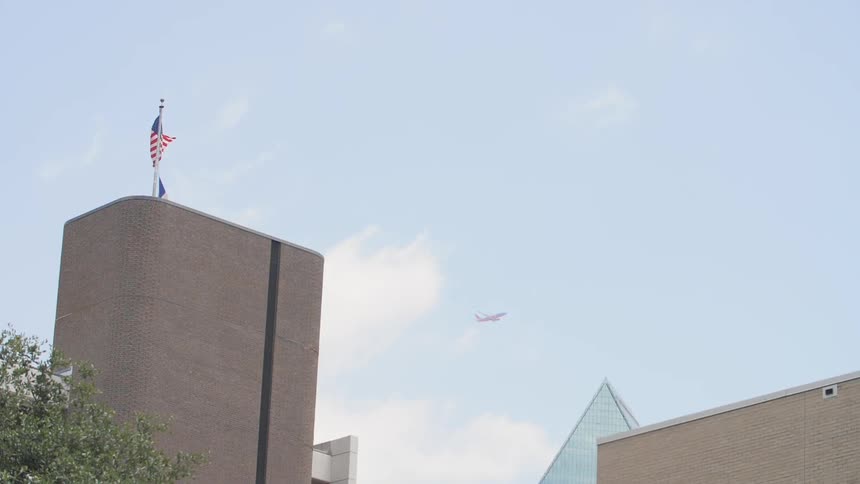 A plane flies high the sky while an american flag waves