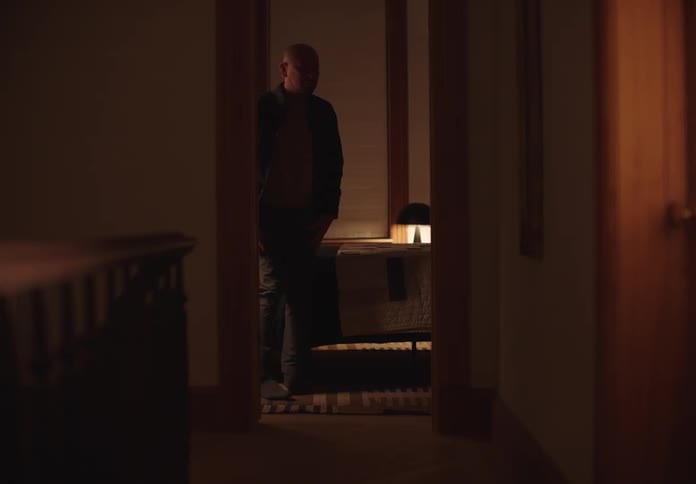 Bald man sitting on his bed stands and walks past the doorway