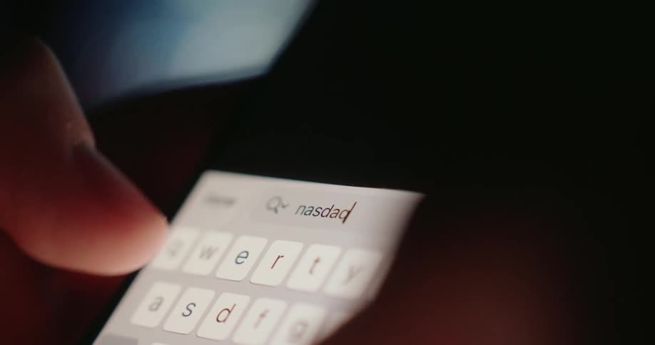 Fingers type on a brightly illuminated smartphone keyboard in a dimly lit area