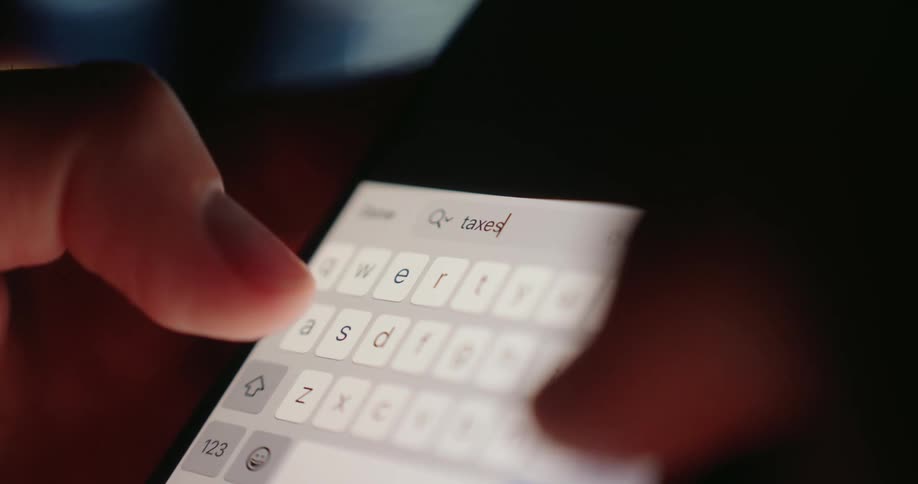 A person types the word taxes into their cell phone in the dark