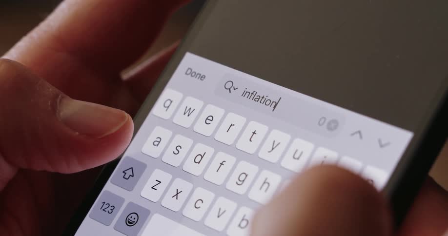 Fingers type the word inflation on a brightly illuminated smartphone keyboard