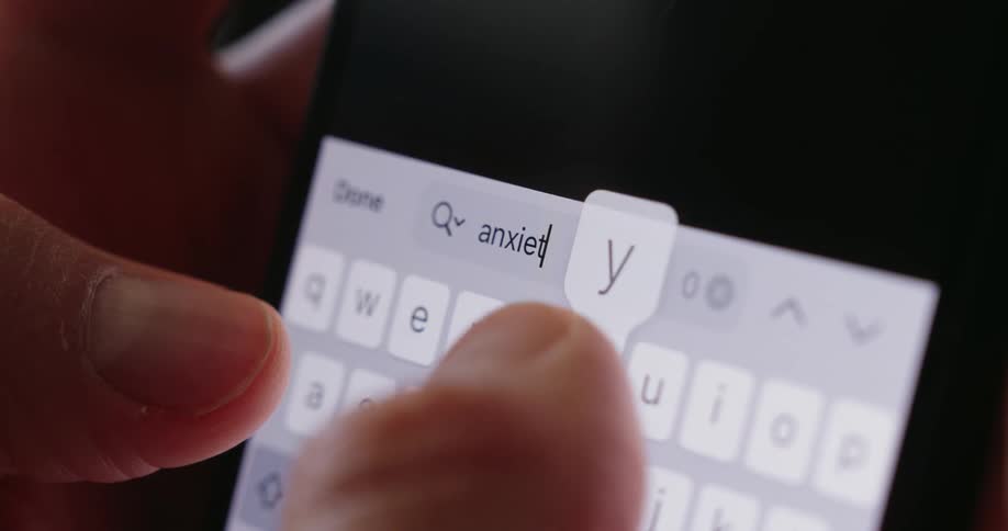 Fingers type on a brightly illuminated smartphone keyboard in a dimly lit area