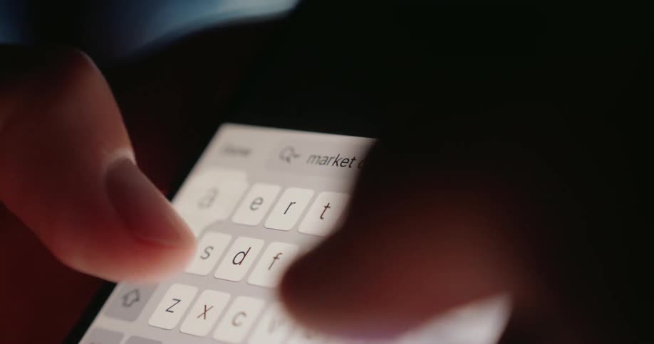 Fingers typing market crash on a smartphone keyboard in low light