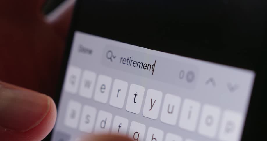 Fingers type the word retirement on a brightly illuminated smartphone keyboard