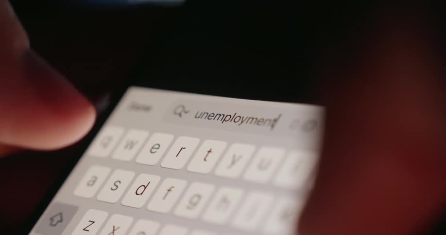 A person types the word unemployment in their mobile device