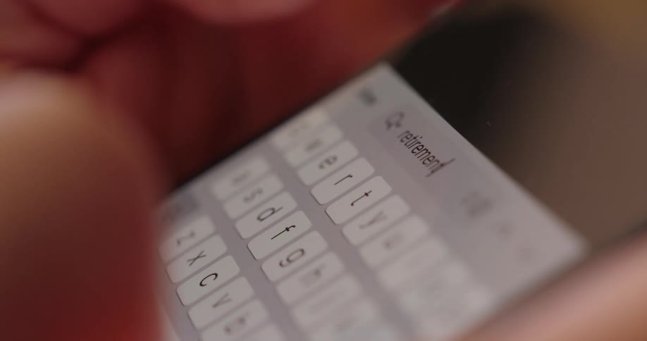 Fingers type the word retirement on a brightly illuminated smartphone keyboard