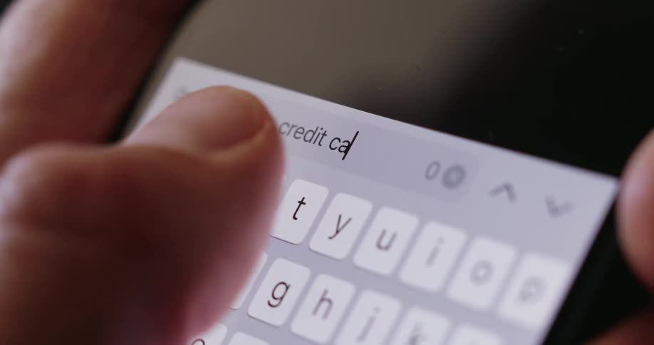 A closeup shot shows fingers typing the words credit card into a search bar on a smartphone screen