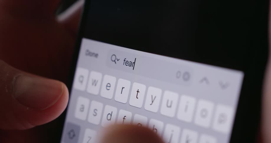 Fingers type the word fear on a brightly illuminated smartphone keyboard