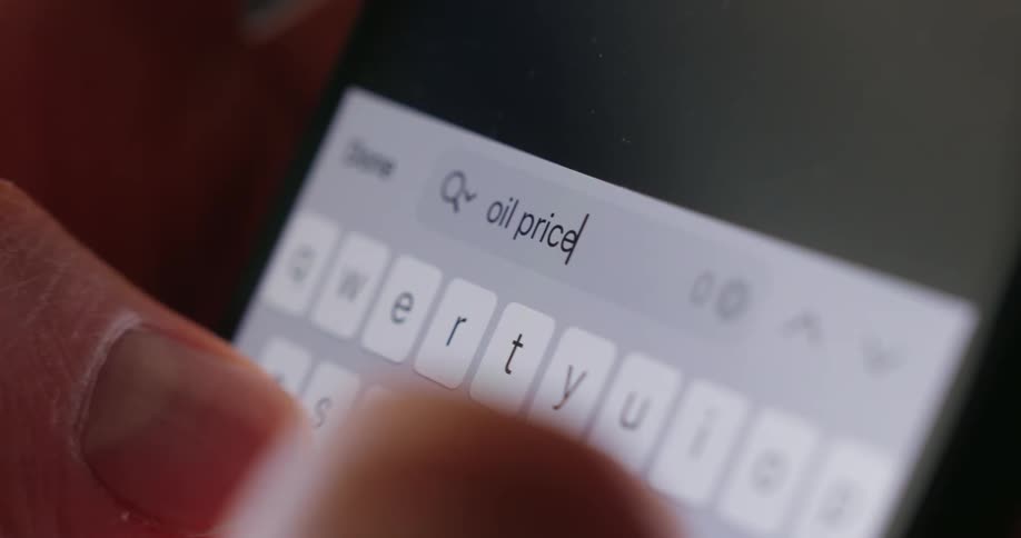 A persons hand holds a smartphone typing the text oil prices