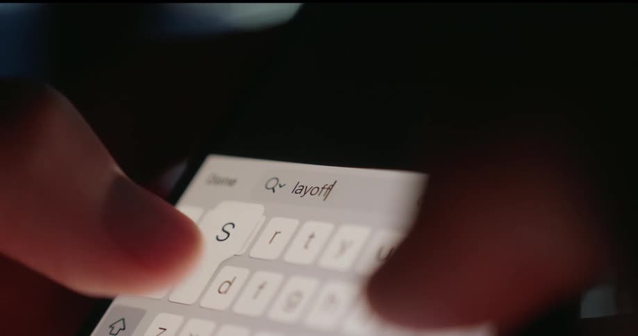 A person types layoffs into a phone search bar suggesting concern