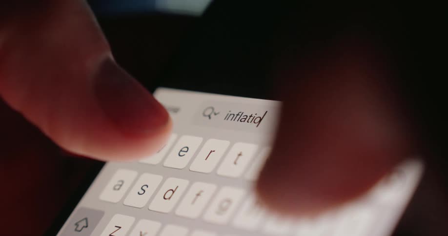 A closeup of a finger typing the word inflation on a smartphone keyboard