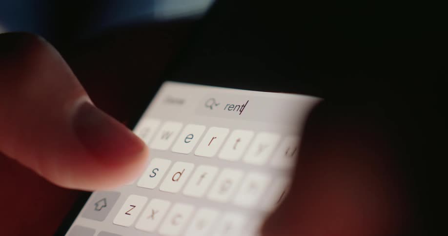 Fingers type on a brightly illuminated smartphone keyboard in a dimly lit area