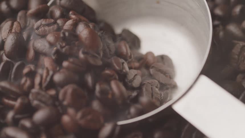 Extreme close up of metal measuring spoon scooping up coffee beans