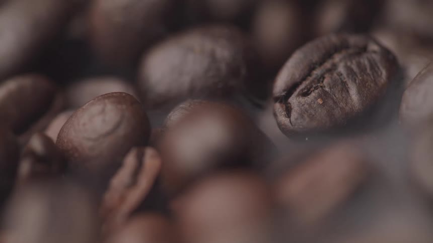 Vapor rises from dark roasted coffee beans