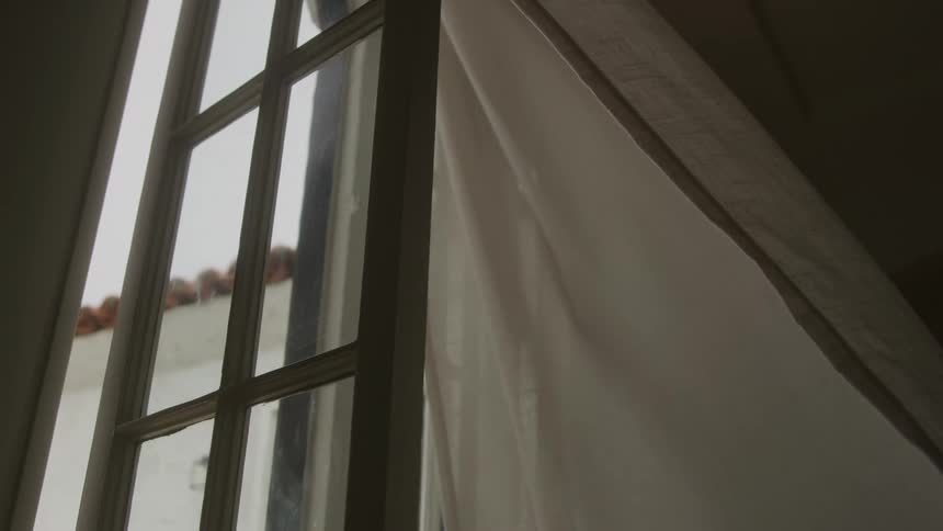 The wind blows through an open window at midday causing the curtain to billow gently