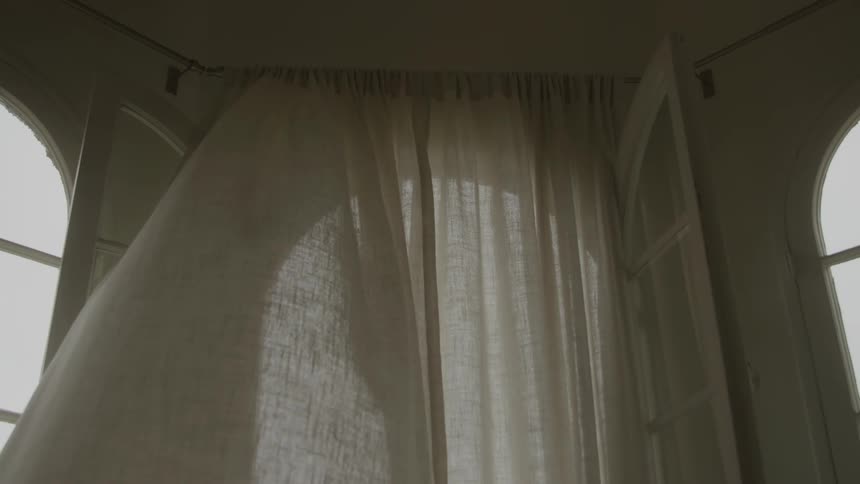 An open window with curtains blowing in the wind at midday
