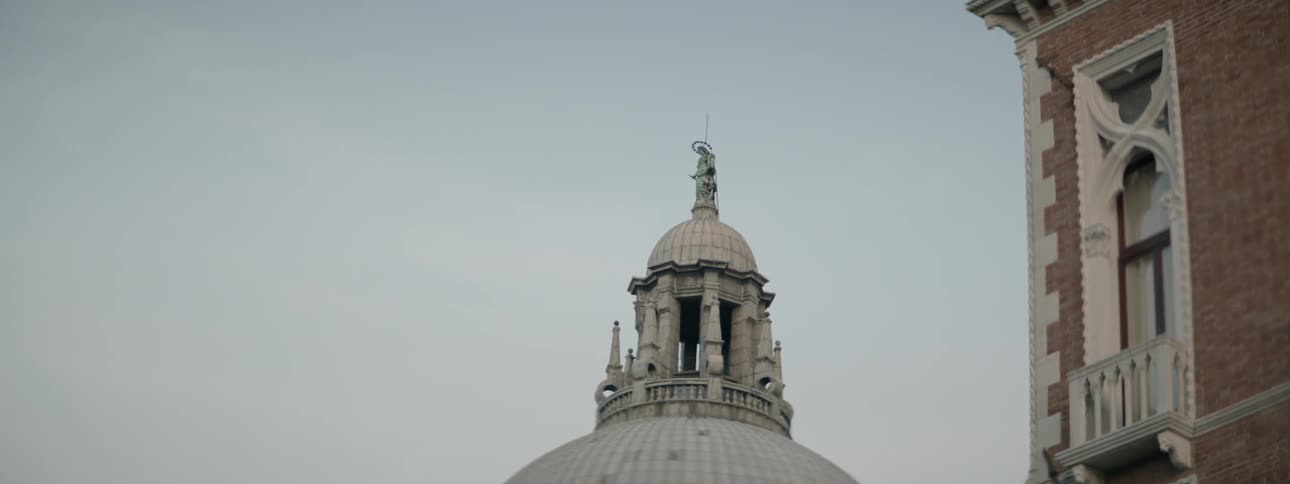 A large building with a dome and religious statue on top behind another building