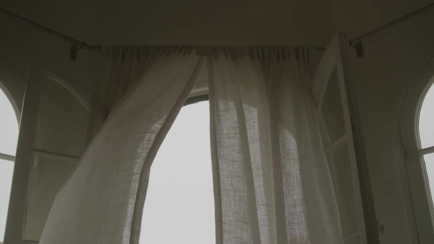 Light sheer curtains billow gently in the wind from an open window in a room