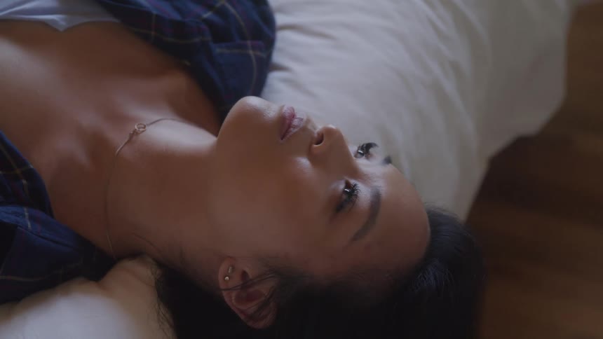 A woman is lying on her back in bed gazing upward with a contemplative expression
