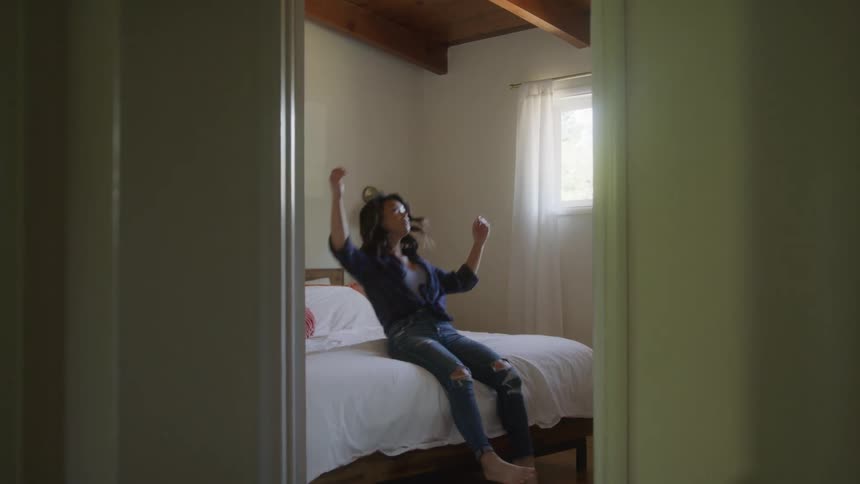 A woman walks into her bedroom and falls backward onto her bed