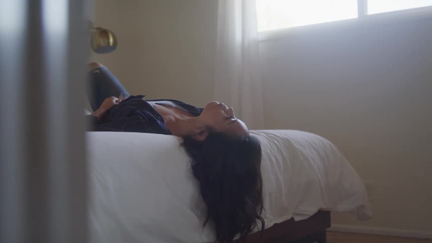 Woman lies on her bed with her hair hanging over its end during the daytime