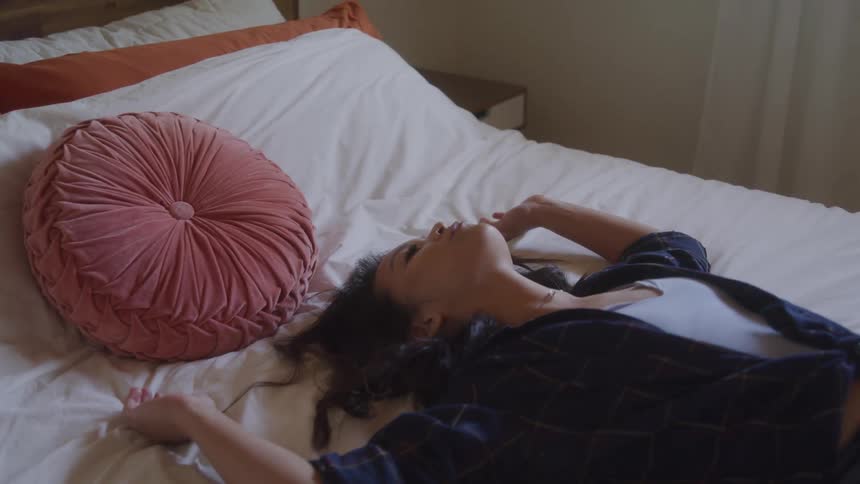 A woman lies flat on her back on the bed covered with a white bedsheet