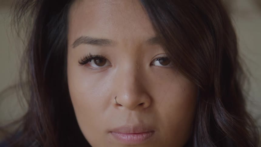 The face of a young woman staring straight ahead and she has a nose piercing