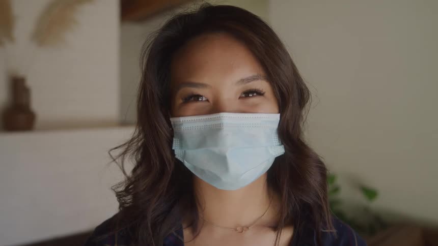 The face of a young woman wearing a white face mask on her mouth and she has happy eyes