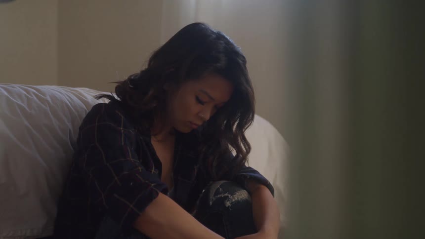 A woman sitting in a room head down and looking sad