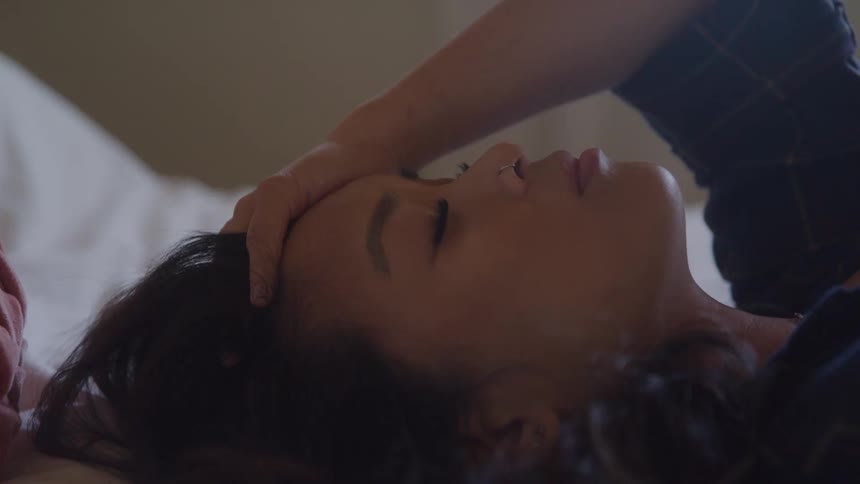 A woman lies in bed with her hand on her forehead appearing emotionally drained