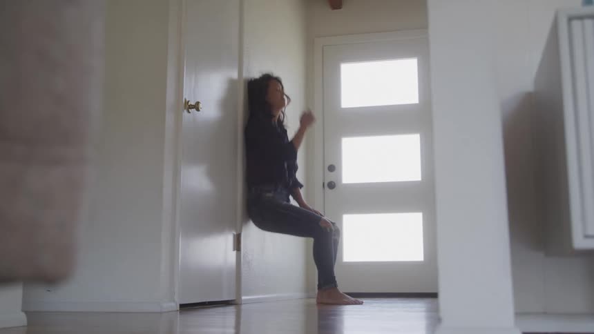 A woman sits alone on the floor in a brightly lit entryway appearing sad and withdrawn after walking around the room