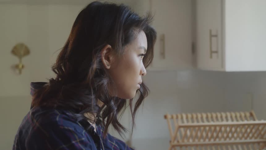 A sad woman is standing in the kitchen