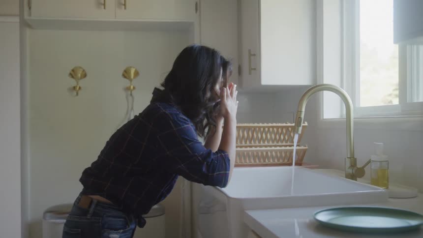 A distressed woman leans over the kitchen sink tossing a plate in frustration