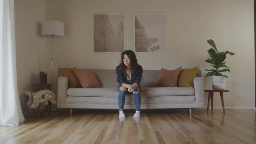 A woman sitting on a living room sofa thoughtful and sad
