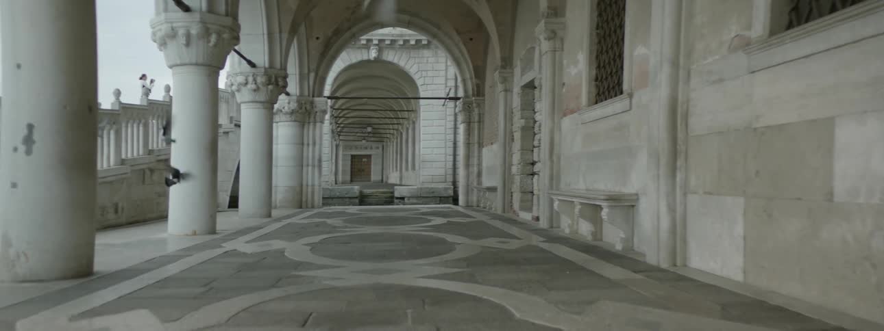 Pigeons fly through a corridor of a building with columns and arches