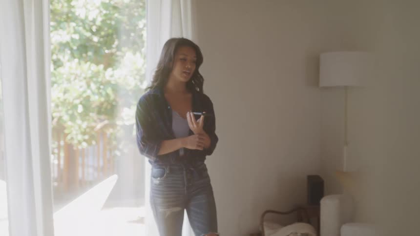 A woman walks back and forth in her living room at midday while talking on the phone