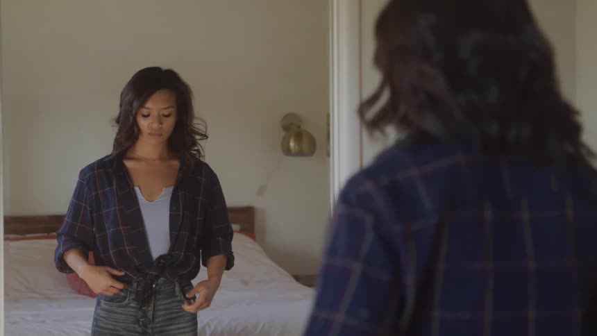 A young woman looks at herself in the mirror while adjusting her hair seemingly lost in thought