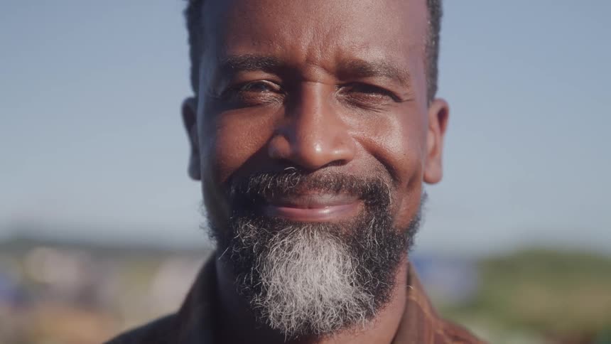 Older bearded man standing outdoors on a sunny day smiles