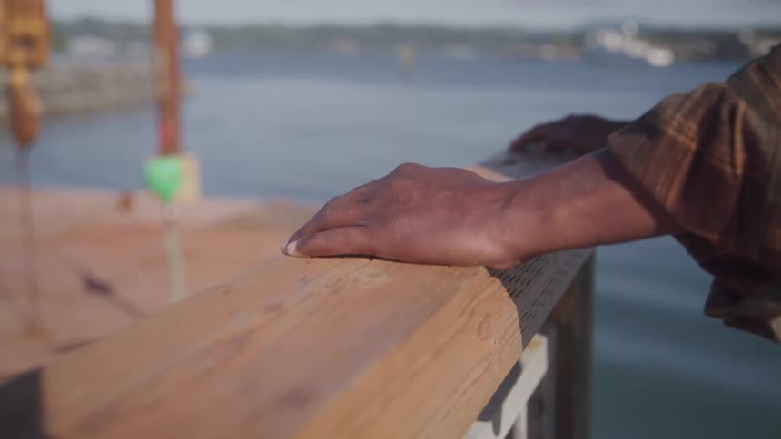 A man is holding a railing by the harbor at midday