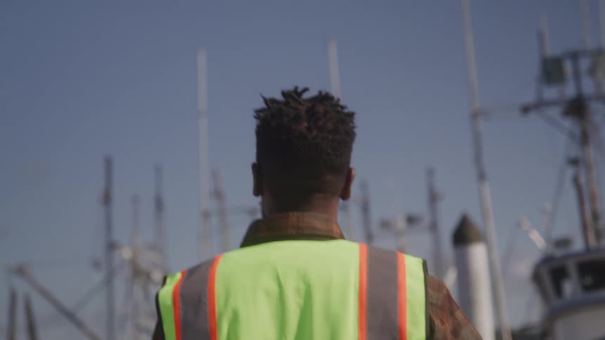 Man wearing an identification vest walking in a marina with parked boats