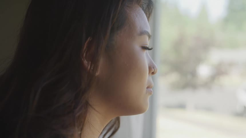 The face of a young woman standing indoors and looking out of a window