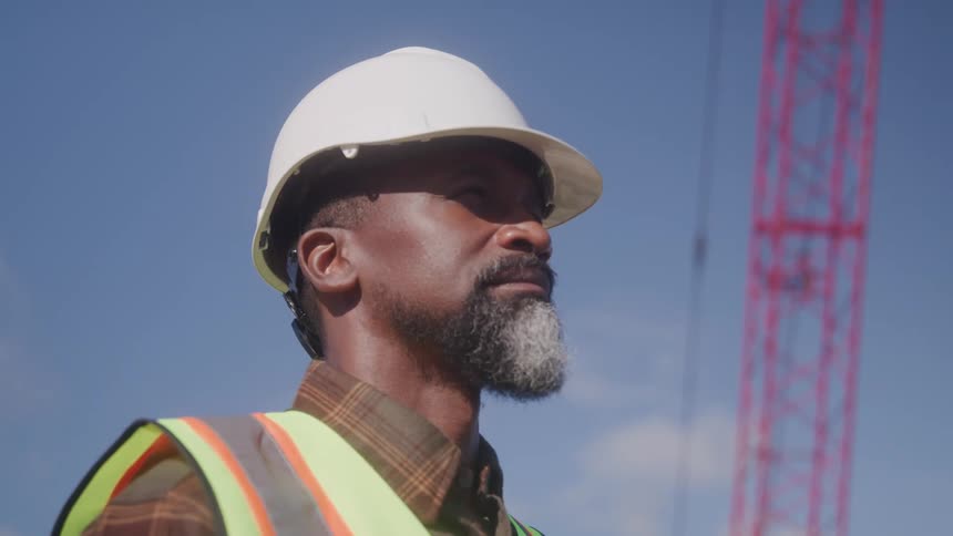 A construction worker with a hard hat stands near a crane