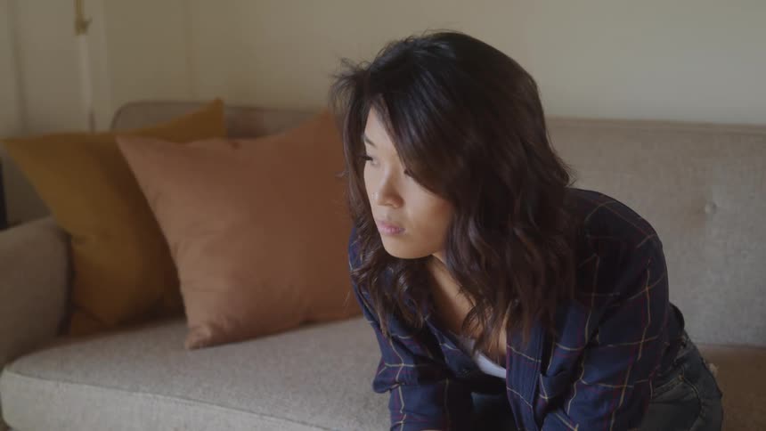 A young woman sits on a couch lost in thought and visibly upset