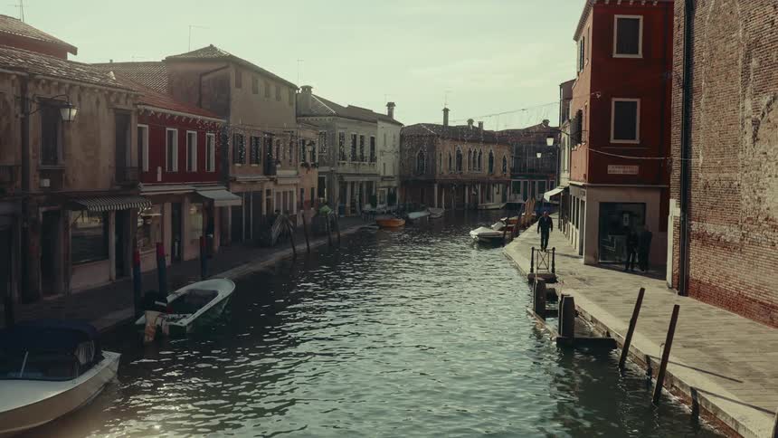A quiet canal with colorful buildings and small boats where a few people walk along the waters edge